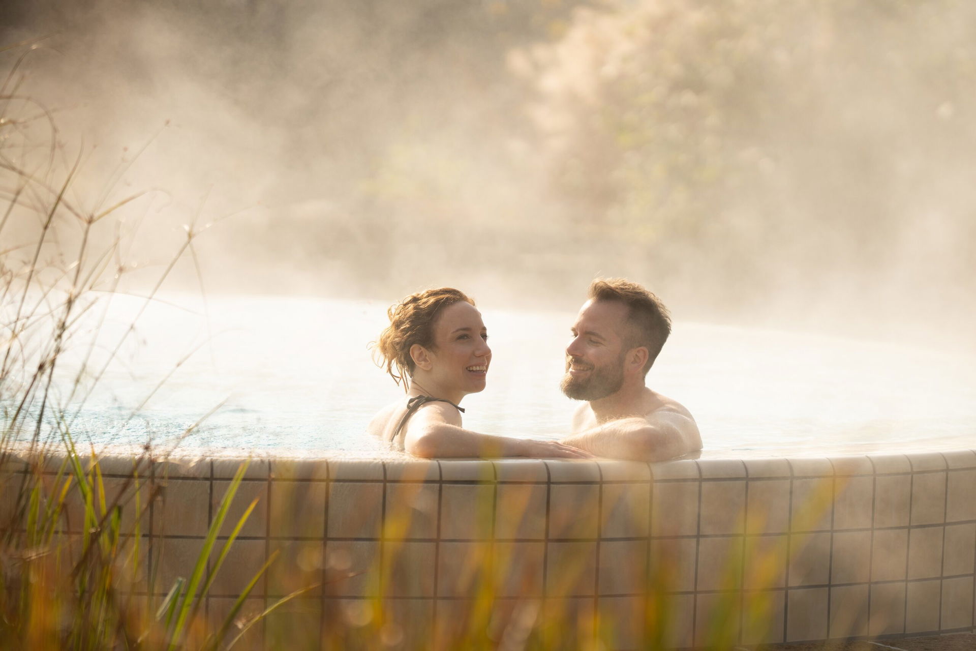 Zwei Personen sitzen im Außenpool einer Therme.