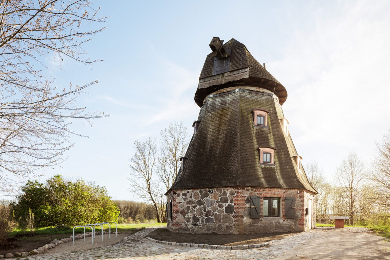 Außenansicht der historischen Schamper Mühle mit Feldstein-Sockel und Holzschindelverkleidung bei Sonnenuntergang