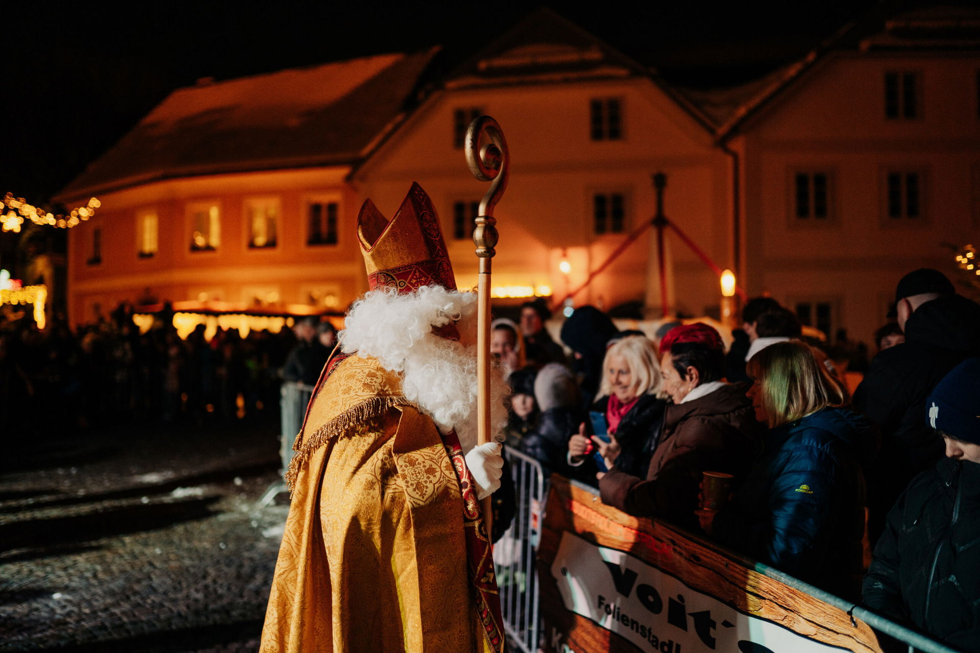 Der Nikolaus trägt seinen roten Bischofsmantel und eine Mitra, während er in einer Hand den goldenen Bischofsstab hält, beim Kramperllauf in St. Florian. Seine majestätische Erscheinung und sein warmes Lächeln stehen im Kontrast zu den furchterregenden Krampusfiguren und verleihen der Veranstaltung eine ausgewogene Mischung aus Fröhlichkeit und Tradition.